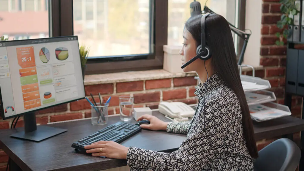 A woman wearing a headset, working at a desk with a computer