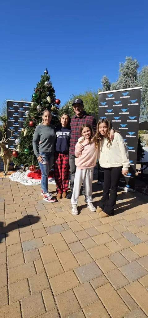 Attendees at a sunny outdoor 'Valley Hopper' holiday event, with a family posing for a picture with a Christmas tree.