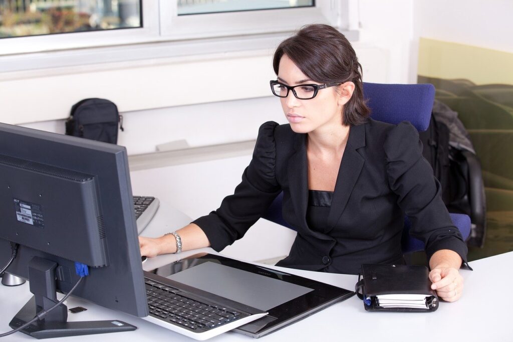 A woman wearing glasses working at a desk with a computer