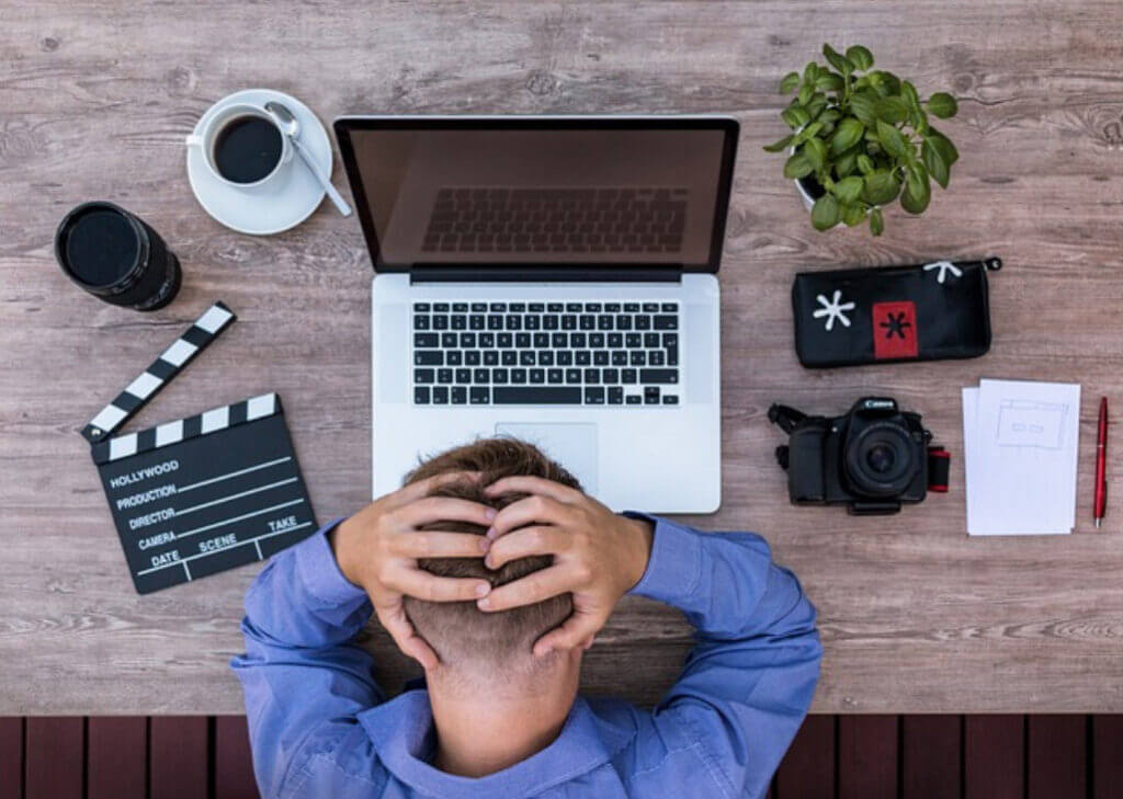 A frustrated man sitting at a desk, using a laptop and camera for work