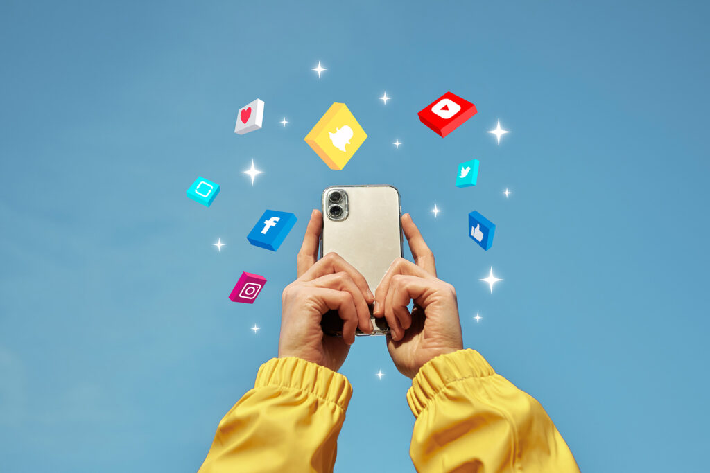 A person holding a smartphone with social media icons flying out of it